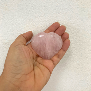 Corazón de cuarzo rosa de 5 cm de ancho sostenido en la mano contra fondo blanco