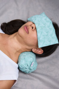 Rollito cervical en uso para aliviar y prevenir el dolor de cuello.  La usuario tiene además una almohadita de ojos.